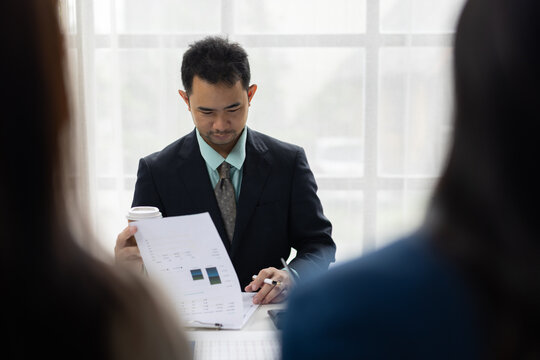 Asian businessman discussing financial report in meeting. Asian businessman presenting financial reports during a corporate meeting, providing data and strategy insights to colleagues.