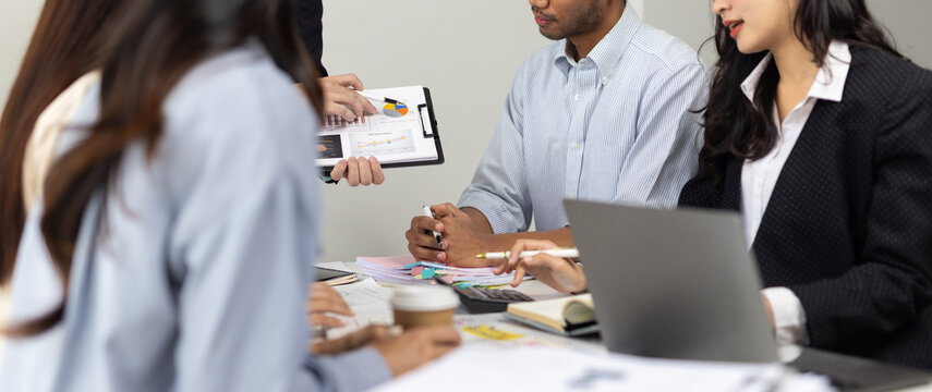 Group of diverse business professionals discussing financial charts and graphs, collaborating on strategy and planning in an office.