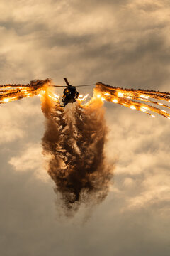 View of an NH-90 helicopter releasing flares during an airshow display, creating a dramatic wing-like pattern of smoke and fire against a cloudy sky in Leszno, Greater Poland Voivod, Poland.