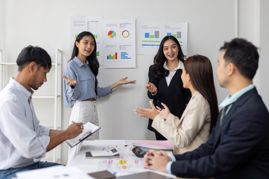 Asian businesswomen presenting data analysis charts in meeting.