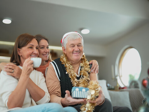 Senior parents and adult daughter sharing Christmas gifts at home, smiling together while enjoying family bonding, holiday celebration and festive tradition.