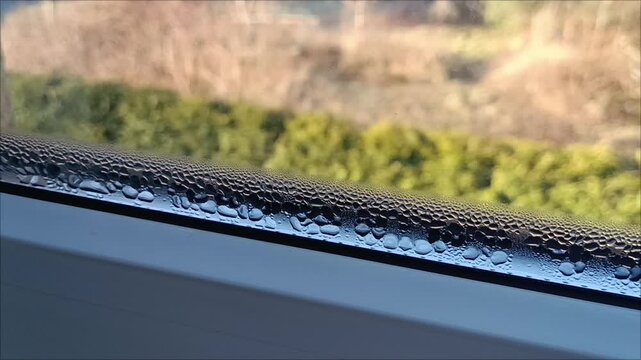 Water drops condensation on bottom edge of plastic window pane, humidity and thermal insulation problem concept with blurred outdoor view.