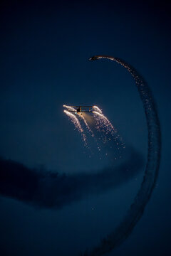 View of a biplane performing night aerobatics with pyrotechnic sparks trailing in the dark sky at the Antidotum Airshow at Leszno Airport, Leszno, Wielkopolskie, Poland.