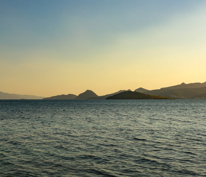 Golden hour light illuminating tranquil sea water and distant islands silhouette against clear sky enjoying peaceful summer evening