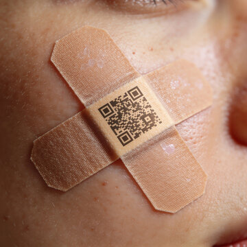 Close‑up artistic shot of a cheek with two crossed bandages and a printed QR code, blending medical symbolism with digital identity in a minimal, modern composition.
