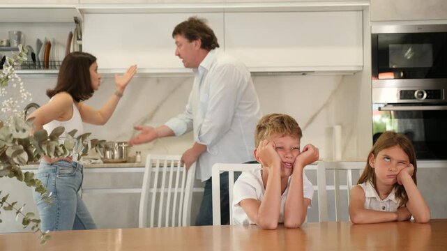  Brother and sister sit at table during conflict between parents