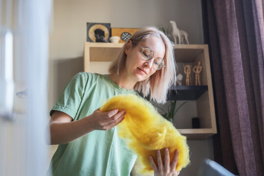 Young Woman With Glasses Shaping Bright Yellow Wool Roving For Handmade Felting In Cozy Home Studio, Using Careful Hands And Focused Expression Beside Shelf Decor, Soft Daylight