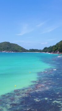 Vertical ascending aerial view over Port Launay in Seychelles revealing turquoise water, tropical coastline, lush vegetation and scenic island landscape.