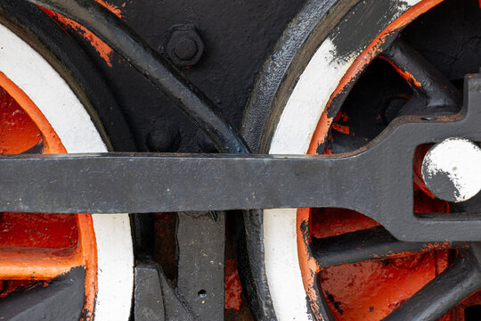 Steam locomotive driving wheels with connecting rod crankpin valve gear and piston linkage on narrow gauge track with ballast. Close view shows mechanical detail for restoration maintenance.