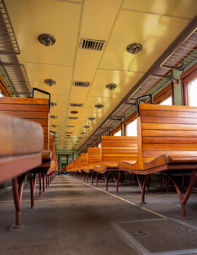 View of the interior of a vintage train carriage featuring rows of wooden benches and overhead luggage racks in Railway Park, Vilnius, Vilniaus apskritis, Lithuania.