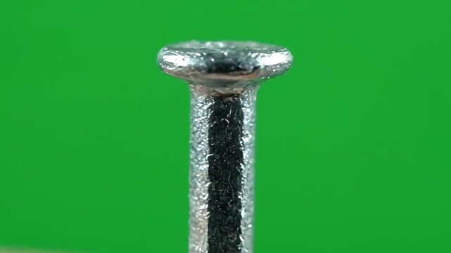 Extreme macro shot of a galvanized steel nail head against a green background