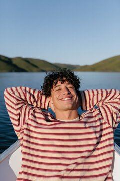 Young man relaxing on a boat at sunset on a calm lake background for banner and summer lifestyle design