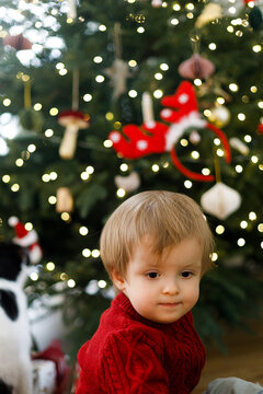 Close Up Portrait of Toddler Boy in Red Knit Sweater against glowing christmas tree. Concept of Wonder and Child Innocence Before Xmas Tree Bokeh Lights