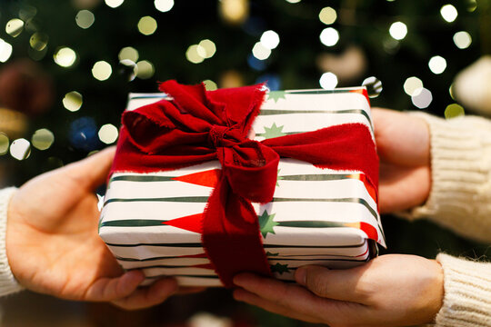 Hands exchanging Christmas present wrapped in striped paper with red ribbon, concept of love and sharing gifts, winter holiday celebration, and cozy festive moments. Merry Christmas
