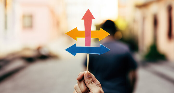 Hand holds colorful directional arrows in a narrow street during daylight