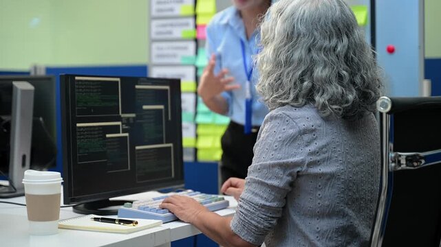 Senior Asian female software engineer coding on a desktop computer while a team member manages project tasks on an agile scrum board