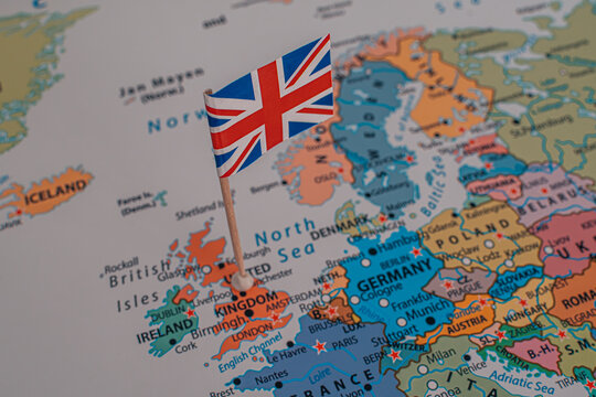 Close-up of a miniature British flag pinned on a political map of Europe over the United Kingdom.