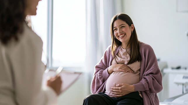 A happy pregnant Asian woman smiling and holding her belly while consulting with her doctor or obstetrician during a prenatal checkup appointment in a clinic.