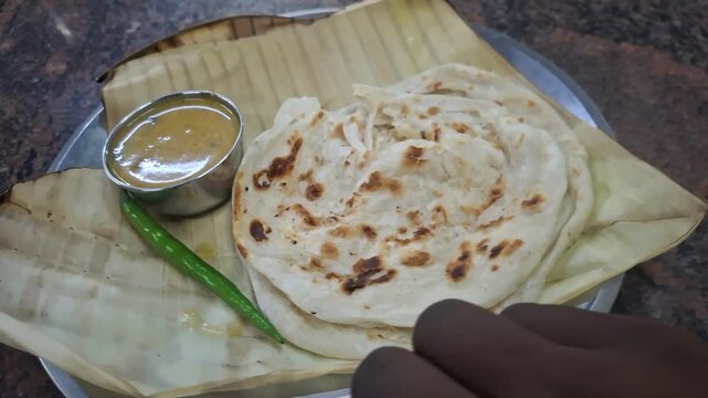 Indian flatbread such as parota or naan served with flavorful gravy in a small bowl, representing traditional South Asian cuisine and delicious dining