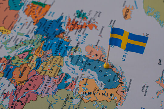 Close-up of a miniature Swedish flag pinned on a political map of Europe over Sweden.