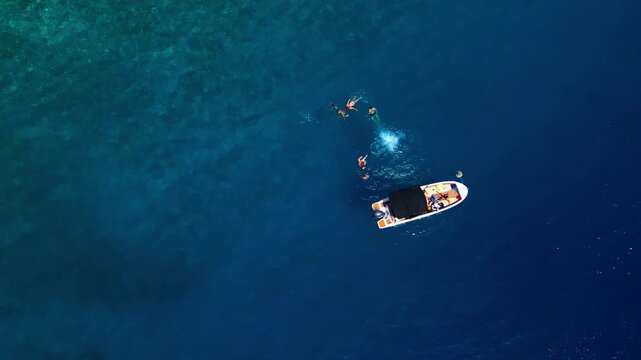 A group of friends enjoys a summer day on the clear, blue waters of the adriatic sea, swimming and relaxing near their small boat anchored close to the coastline.