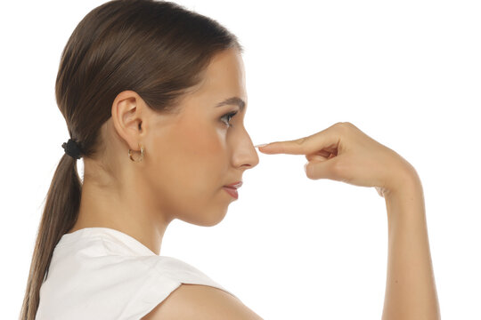 Side profile of a young woman gently touching her nose with finger, rhinoplasty concept, closed eyes, on white background.
