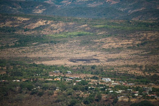 View of the settlement at the base of French Mountain, featuring dry hills, sparse vegetation, and small buildings in Antsiranana, Diana, Madagascar.