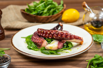 Grilled octopus served on fresh spinach with creamy potato puree, restaurant seafood, side view on a rustic wooden table © Microgen