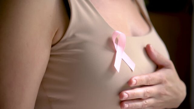 Extreme close-up of hand interacting with pink satin awareness ribbon on clothing, representing compassion during awareness month.