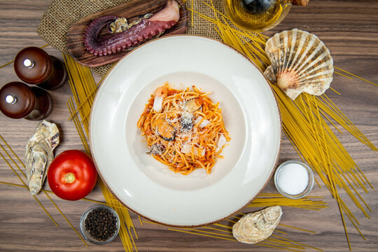 Spaghetti with octopus in tomato sauce topped with parmesan cheese, food flat lay, top-view on a rustic wooden table