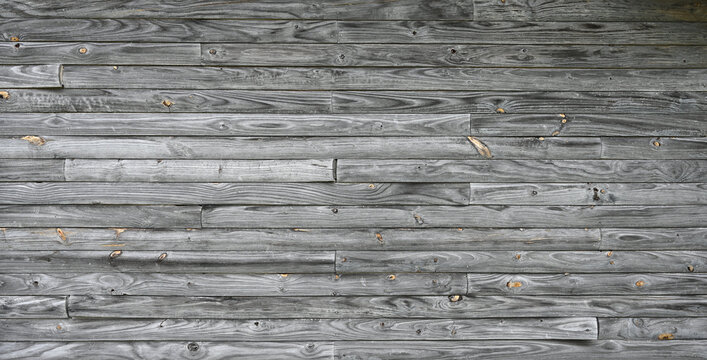 A weathered natural patina drop siding wall surface in a horizontal orientation with rough, unpainted wood planks showing strong grain, knots, curling board ends and dry slats with splits and cracks