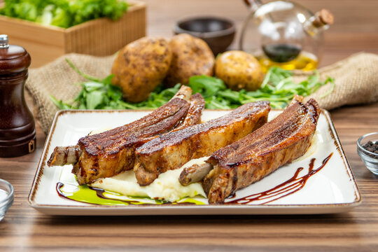 Roasted pork ribs served on creamy mashed potatoes, restaurant main course, side view on a rustic wooden table
