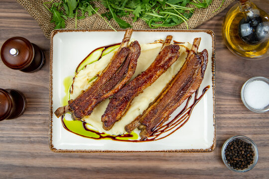 Roasted pork ribs served on creamy mashed potatoes,  top-view on a rustic wooden table