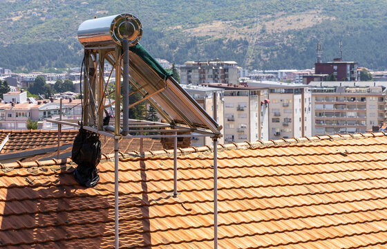 View of a solar water heater installed on a terracotta tiled roof with urban apartment buildings and hills in the background in Ohrid, Municipality of Ohrid, North Macedonia.