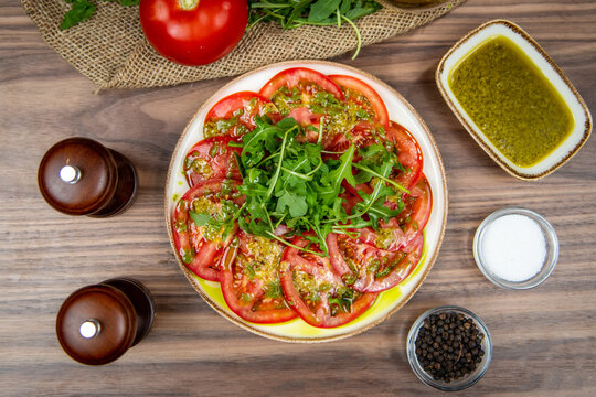Tomato carpaccio with arugula and herb dressing, food flat lay, top-view on a rustic wooden table