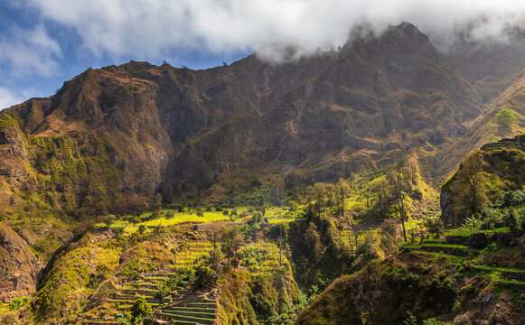 View of the lush terraced fields and dramatic mountain peaks of Santo Antao under a cloudy sky in Faja de Cima, Paul, Cabo Verde.