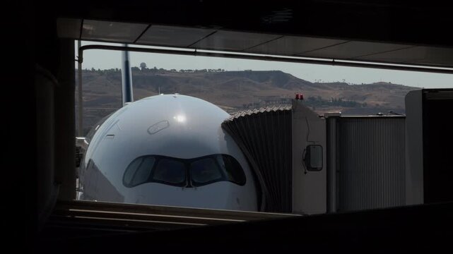 White Airplane Parked at Gate Seen Through Terminal Window