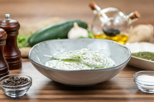 Fresh cucumber salad with creamy yogurt dressing and herbs served in a gray bowl, restaurant side dish, side view on a rustic wooden table