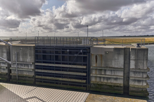 View of the storm sluice gate at Esbjerg Marina, featuring concrete walls, metal gate structure, and metal railings under a cloudy sky in Esbjerg, Denmark.