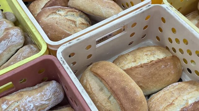 overhead three-quarter view of multiple freshly baked breads packed in stackable perforated plastic crates, showing ciabatta rolls with pale crust and texture bread