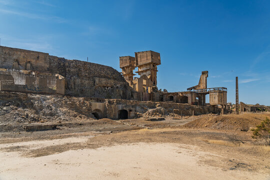 View of the abandoned industrial ruins of Minas de Sao Domingos with stone structures and weathered architecture under a clear blue sky in Corte do Pinto, Beja District, Portugal.
