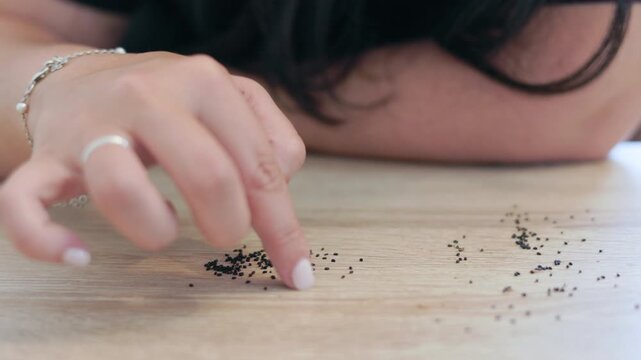 Woman's hand meticulously counting tiny basil seeds on a wooden table, representing concepts of patience, investment, regeneration, urban gardening, and slow living