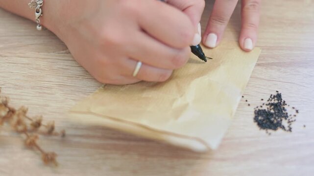 Woman's hand writing the word basil in spanish on a paper seed packet, a symbolic representation of patience, slow living, urban gardening, investment and regeneration