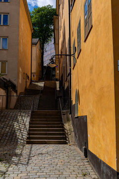 View of a narrow cobblestone street with stairs in Gamla Stan, flanked by historic yellow buildings and a vintage street lamp in Stockholm, Stockholm County, Sweden.