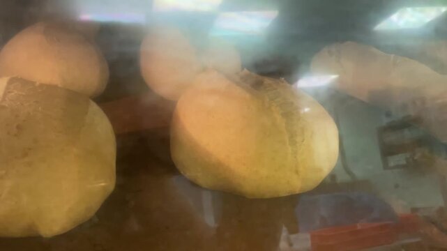 Closeup of yeast pastries baking inside a commercial oven, viewed through fogged glass. Fresh bread rolls rise under heat in a professional bakery, artisanal baking and food production.