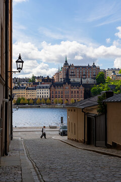 View of historic waterfront architecture and a cobblestone street with a pedestrian in Stockholm, Stockholm County, Sweden.