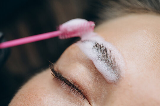 Close-up of a beauty specialist applying lamination solution to a clients eyebrow with a spoolie brush during a professional brow treatment.