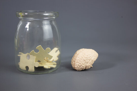 Toy brain and puzzle pieces inside a glass jar, symbolizing the search for ideas, inspiration, memory, creativity, problem solving, cognitive thinking, learning, mental focus, and discovering new solu