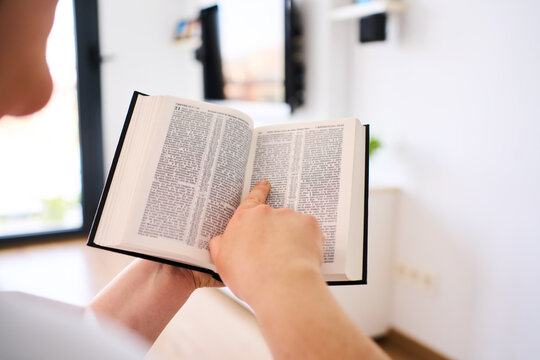 Person, bible book and point with hands, reading or studying for praise, worship or faith in home. Knowledge, closeup and information with religion, learning or spiritual guide for connection to God