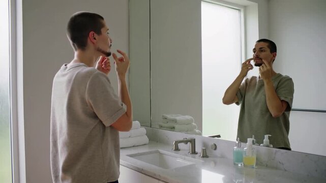 Reaching man flossing teeth at home sink, using floss pick and checking mirror for oral care